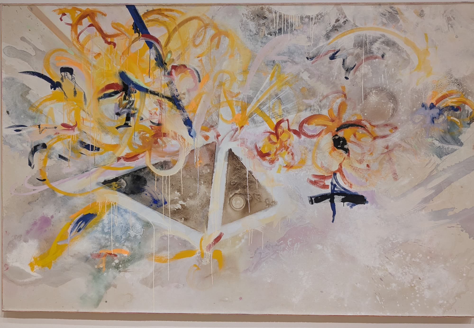 An abstract painting with swirling yellow, orange, and blue brushstrokes around a metallic triangular form on a pale ground